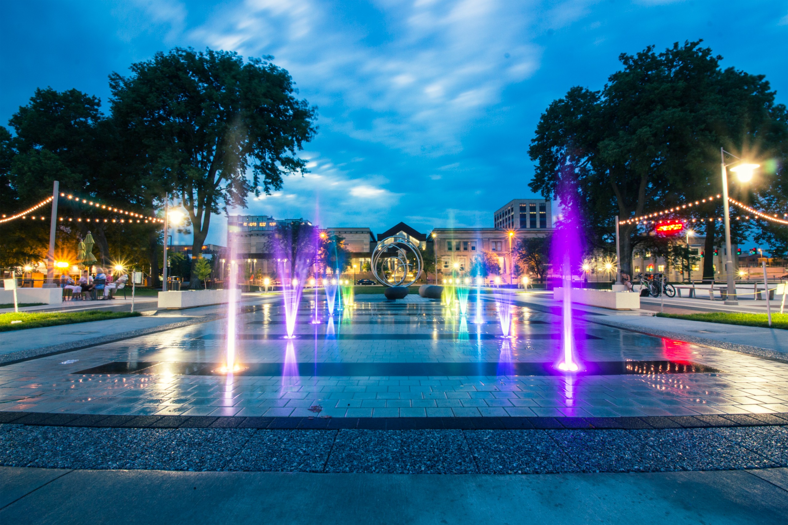 This photo showcases Green Square in the evening, with water and colored lights.