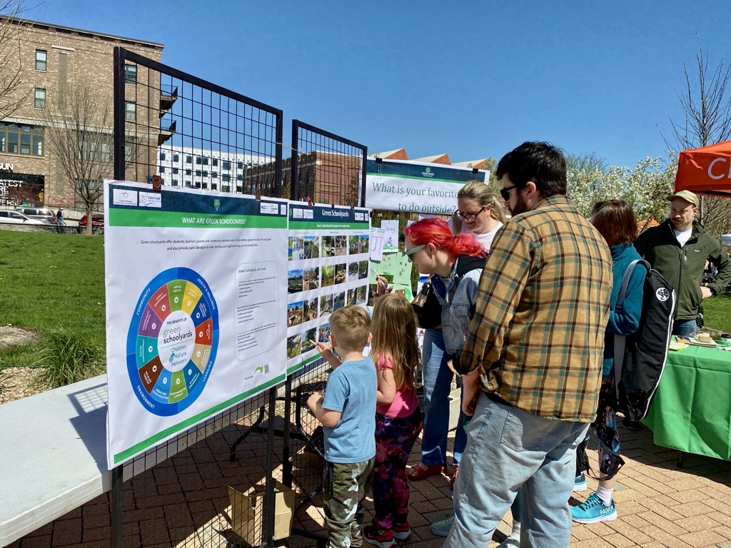 People engaging with boards at the Nature Everywhere EcoFest 2025 event. The boards are colorful and provide information, and adults and children alike are learning and engaging with the content.